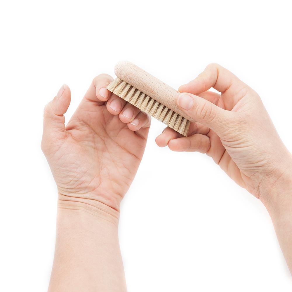 Hands holding natural wooden nail brush, brushing and scrubbing cuticles.