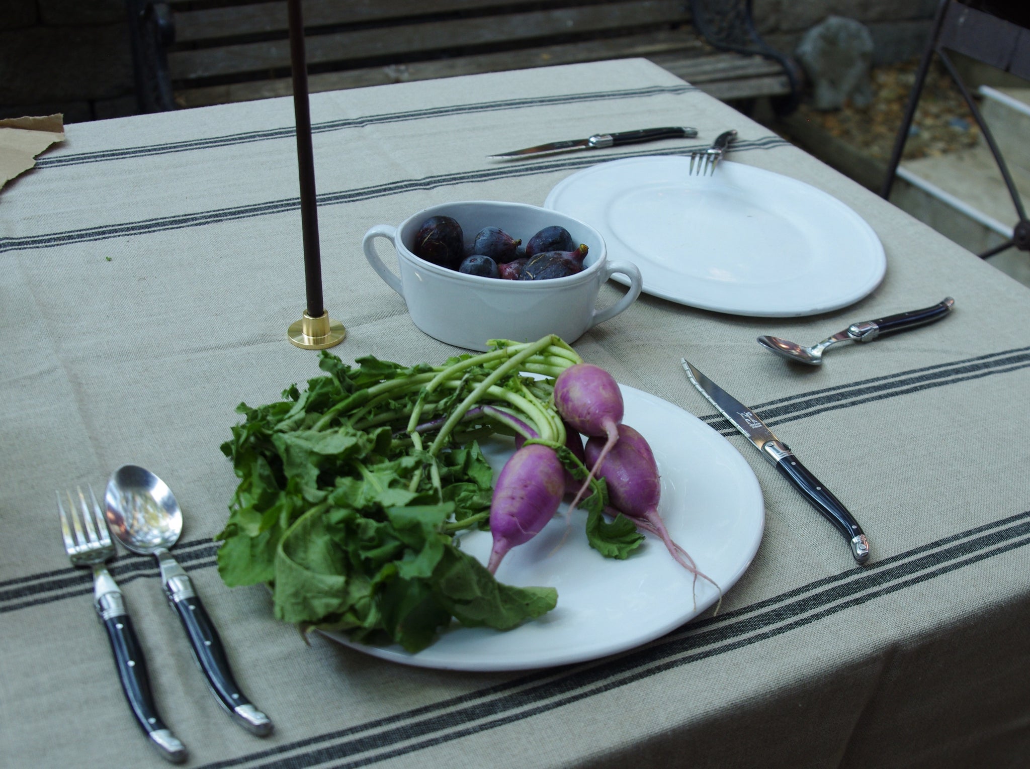 Outdoor table seting featuring white ceramic dinner plates and black cutlery.