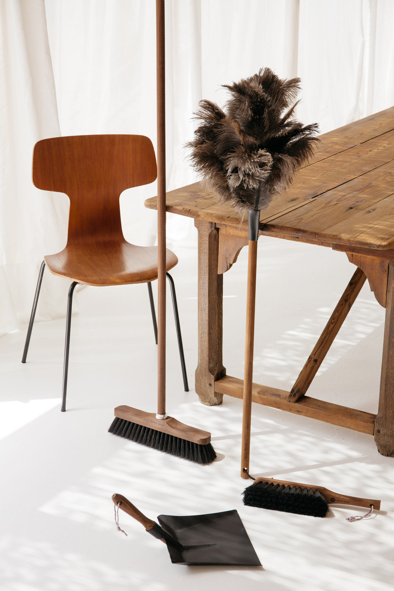 Feather duster with long wood handle next to wooden broom and hand brush as well as dustpan with wooden handle.