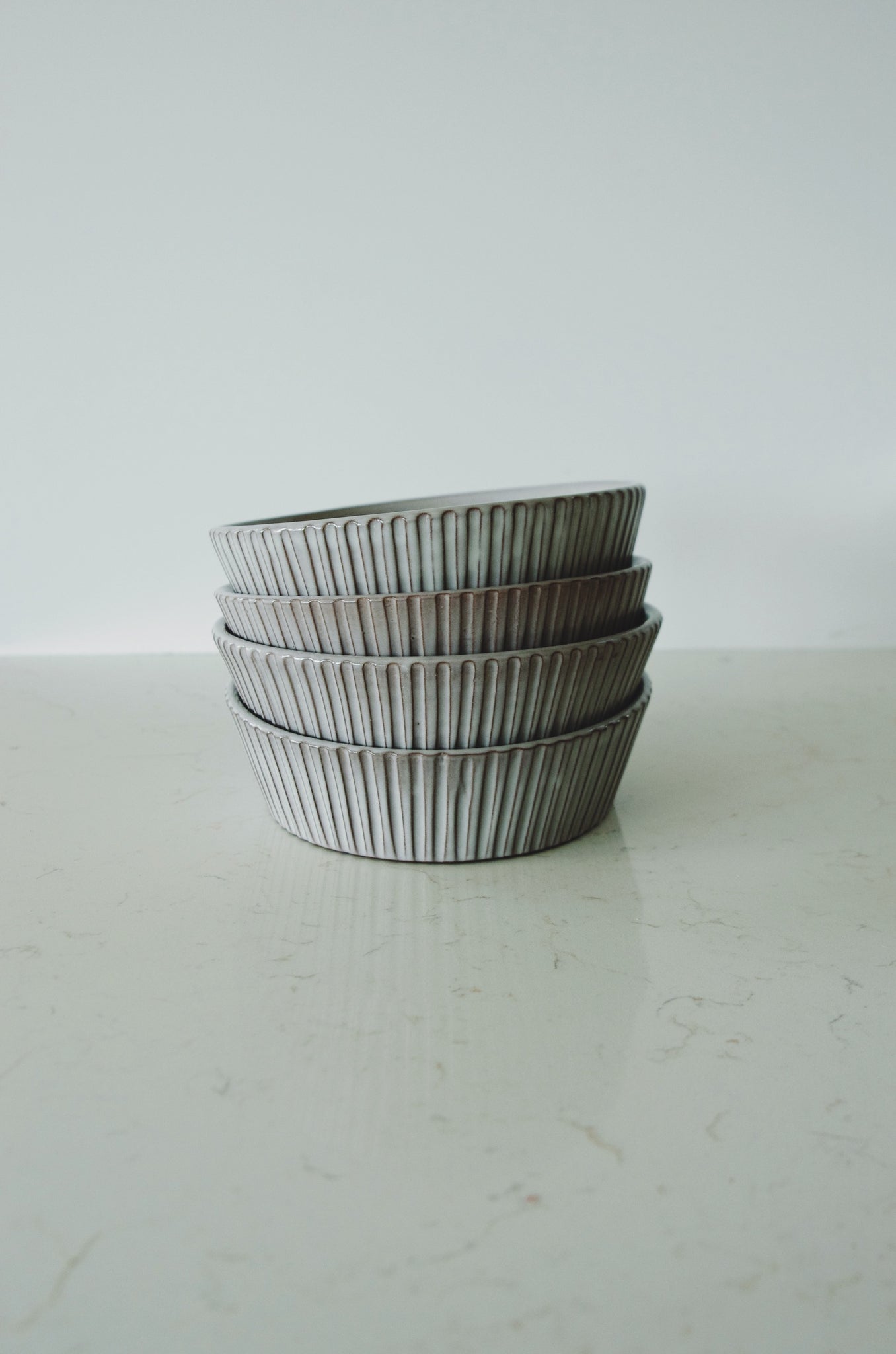A stack of grey ribbed ceramic bowls on a marble countertop with a plain white background.