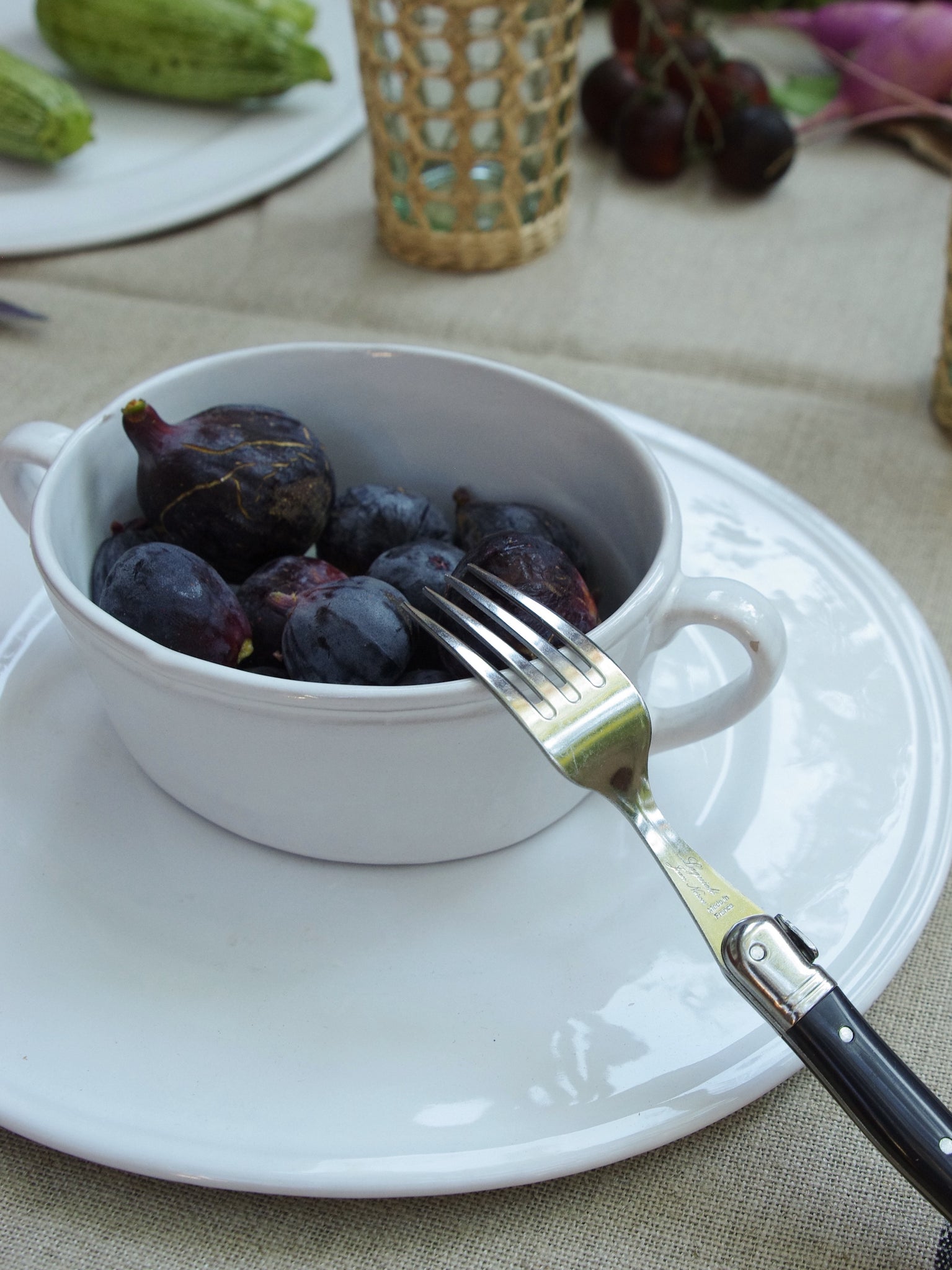 Bowl with two handles holding a bowl of figs next to a fork with a black handle.