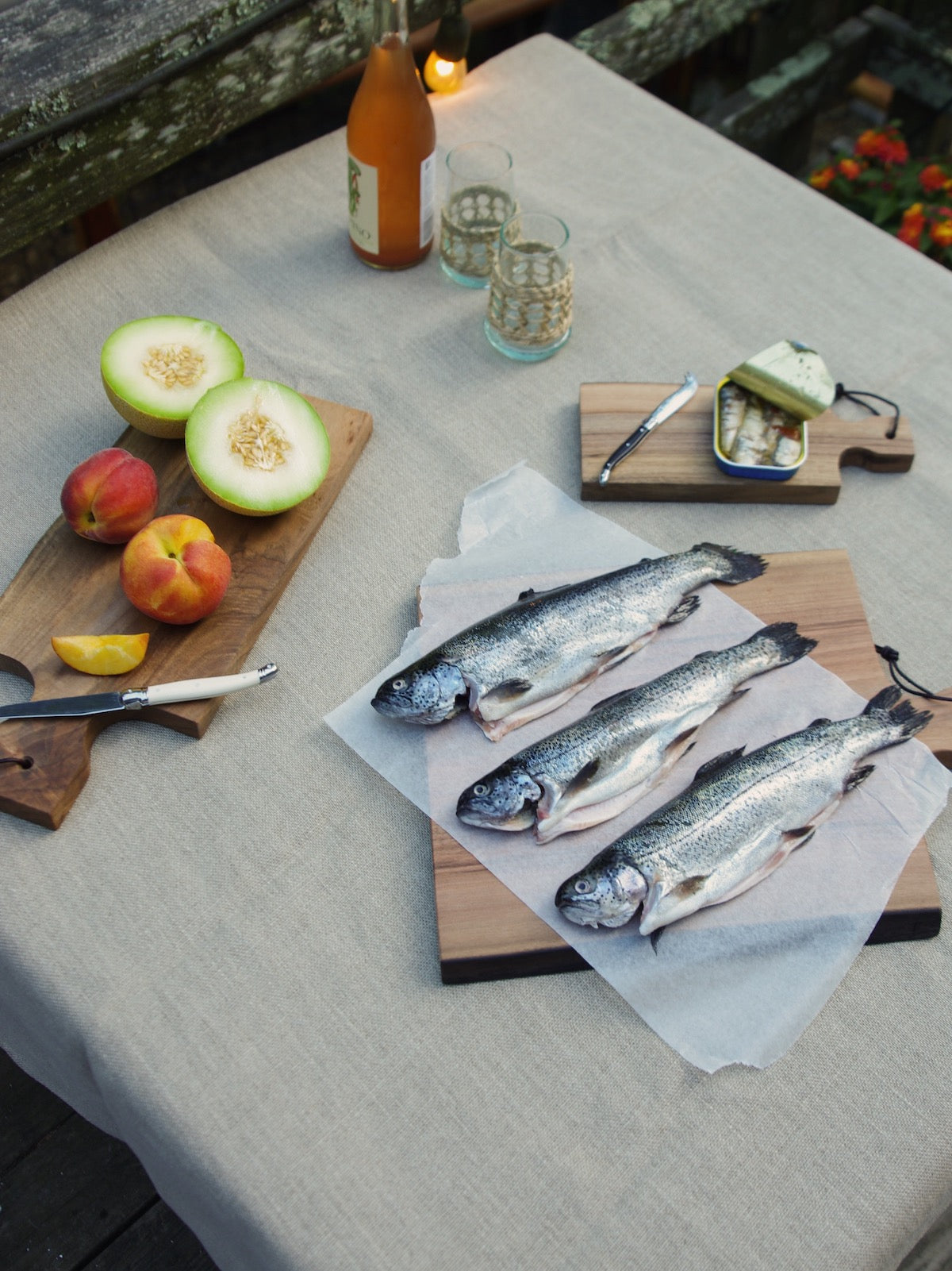 Fish on wooden cutting board. Cut fruit and knife on medium board. Sardines on small wooden cutting board.