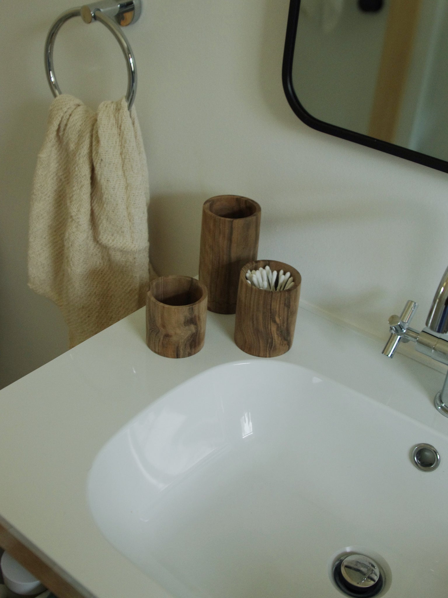 Three wooden cups in a bathroom holding q-tips.