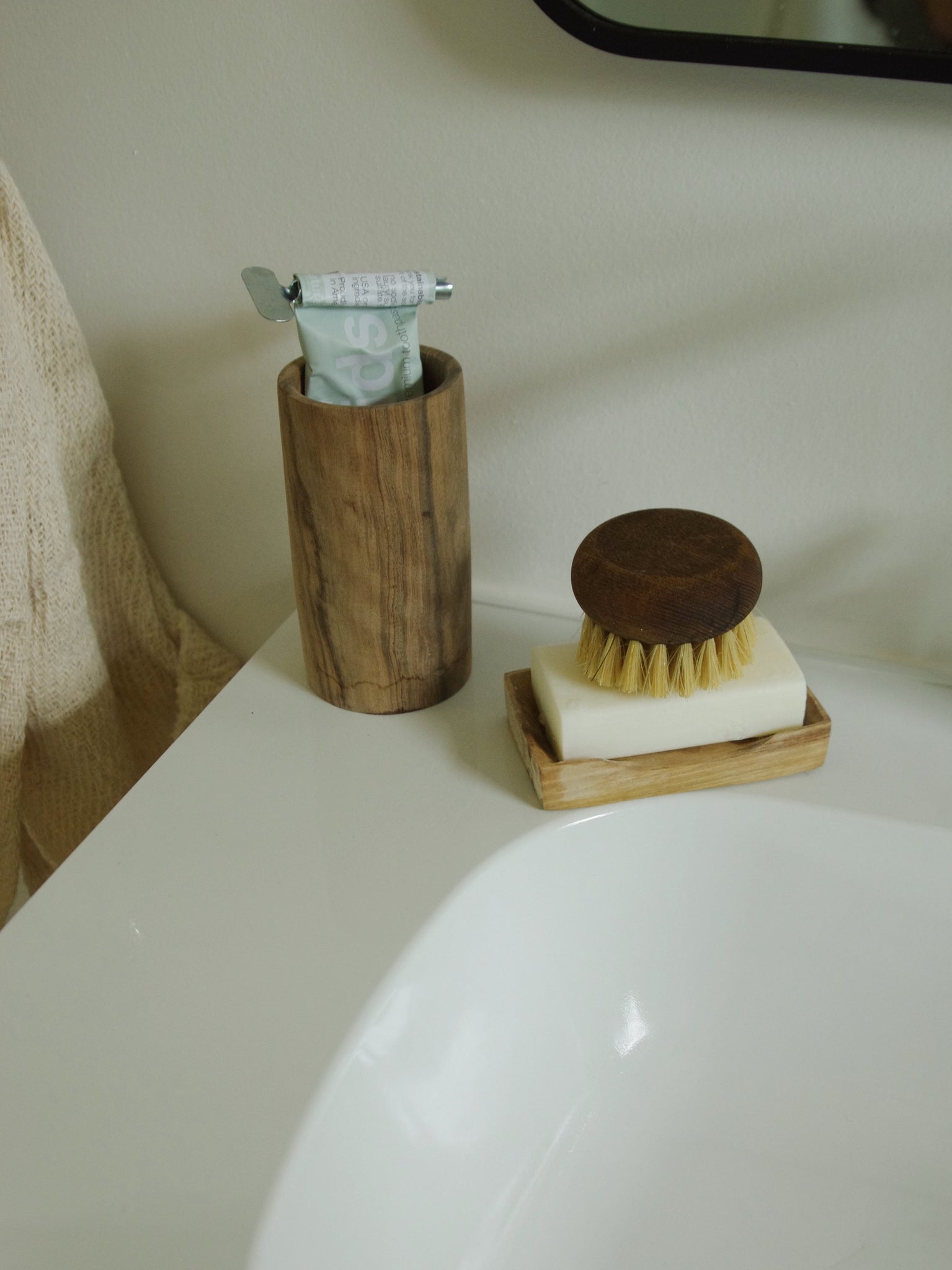 Wooden cup holding toothpaste next to wooden soap tray.