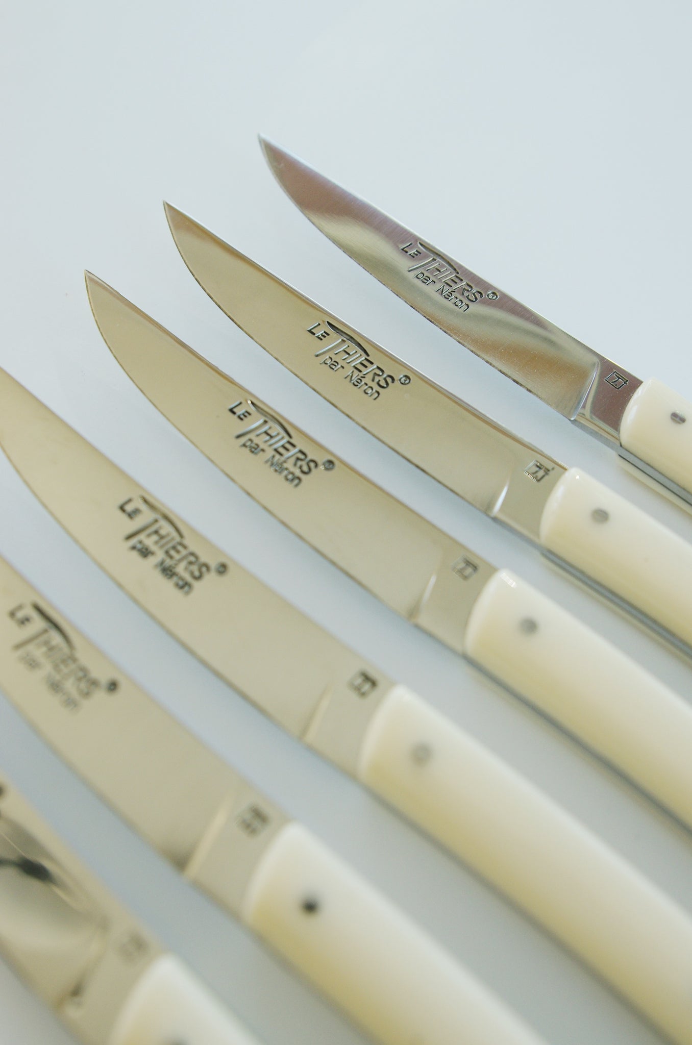 Row of knives that read 'Le Thiers par Neron' with ivory colored handles.