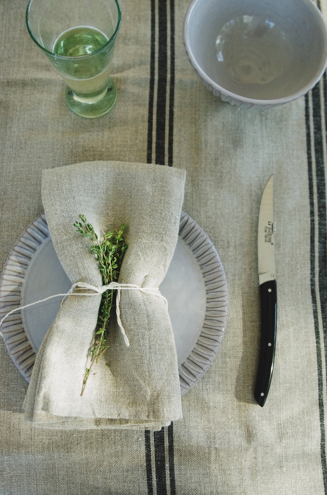 Tied linen napkin with herbs on plate with ridged edges next to small knife with black handle.