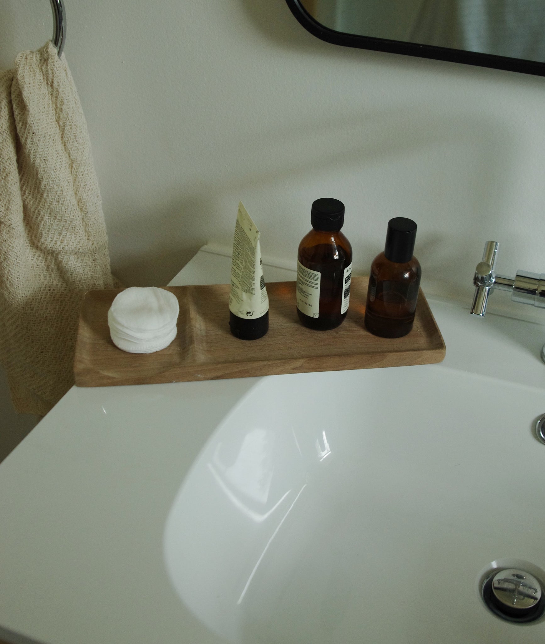 Wooden bathroom tray holding cotton pads and skincare bottles.