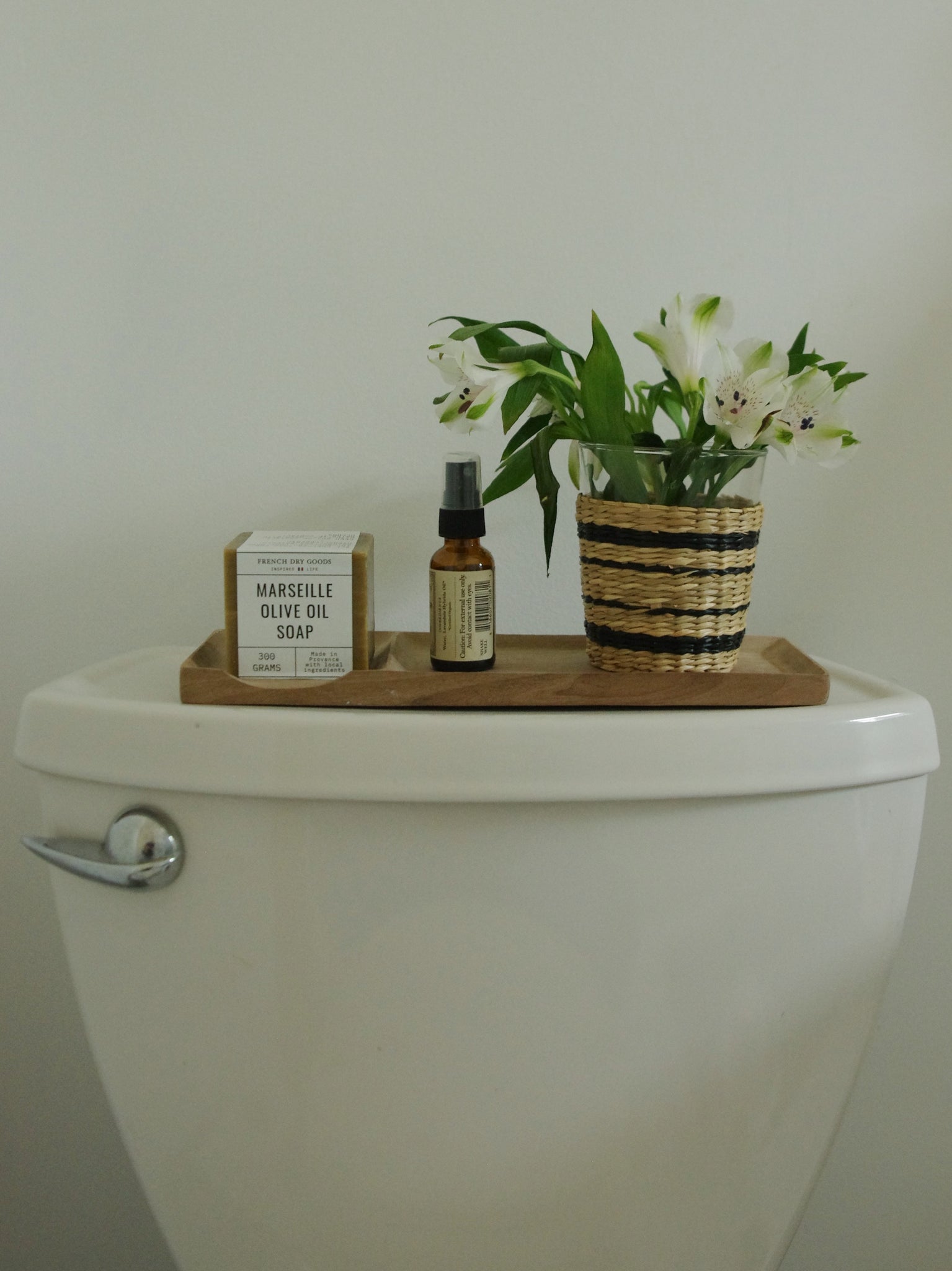 Wooden bathroom tray holding soap, spray, and flowers.