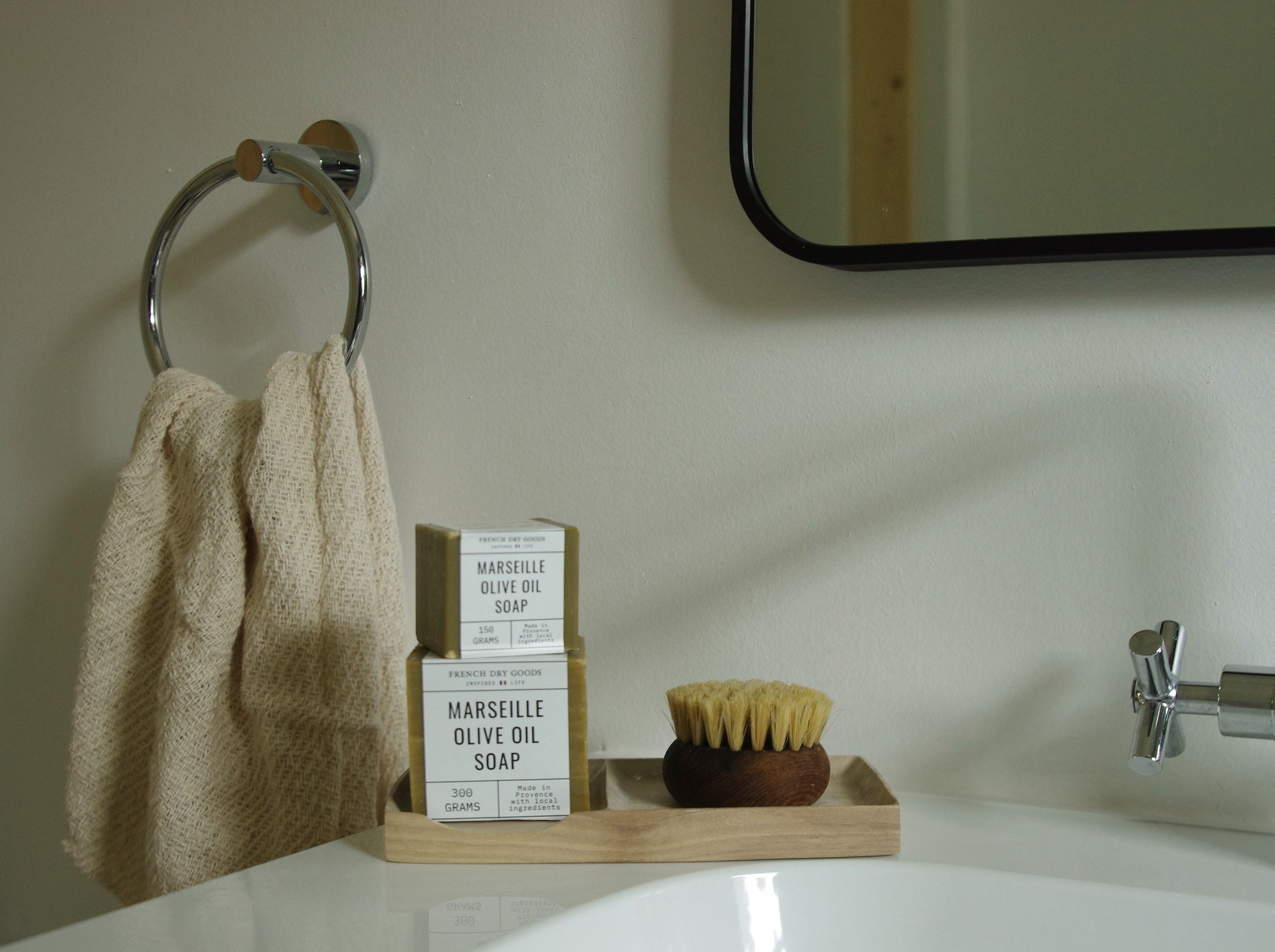 Wooden bathroom tray holding scrub brush and stack of two Marseille soap cubes.