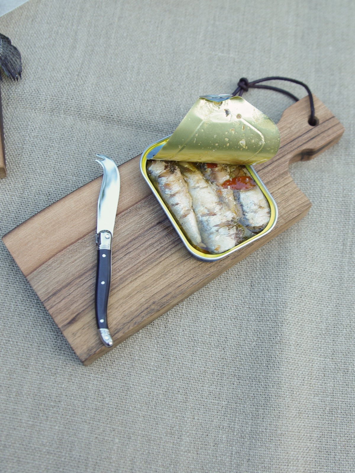 Sardines and knife on small walnut board.
