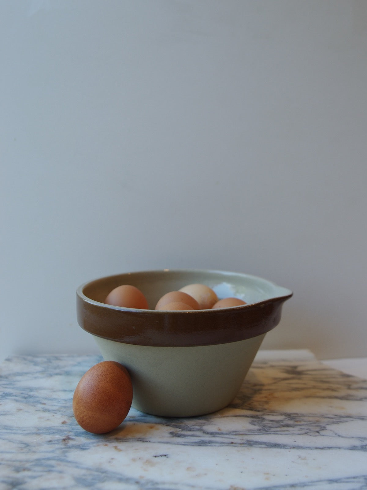 Brown and cream colored mixing bowl with spout full of eggs.