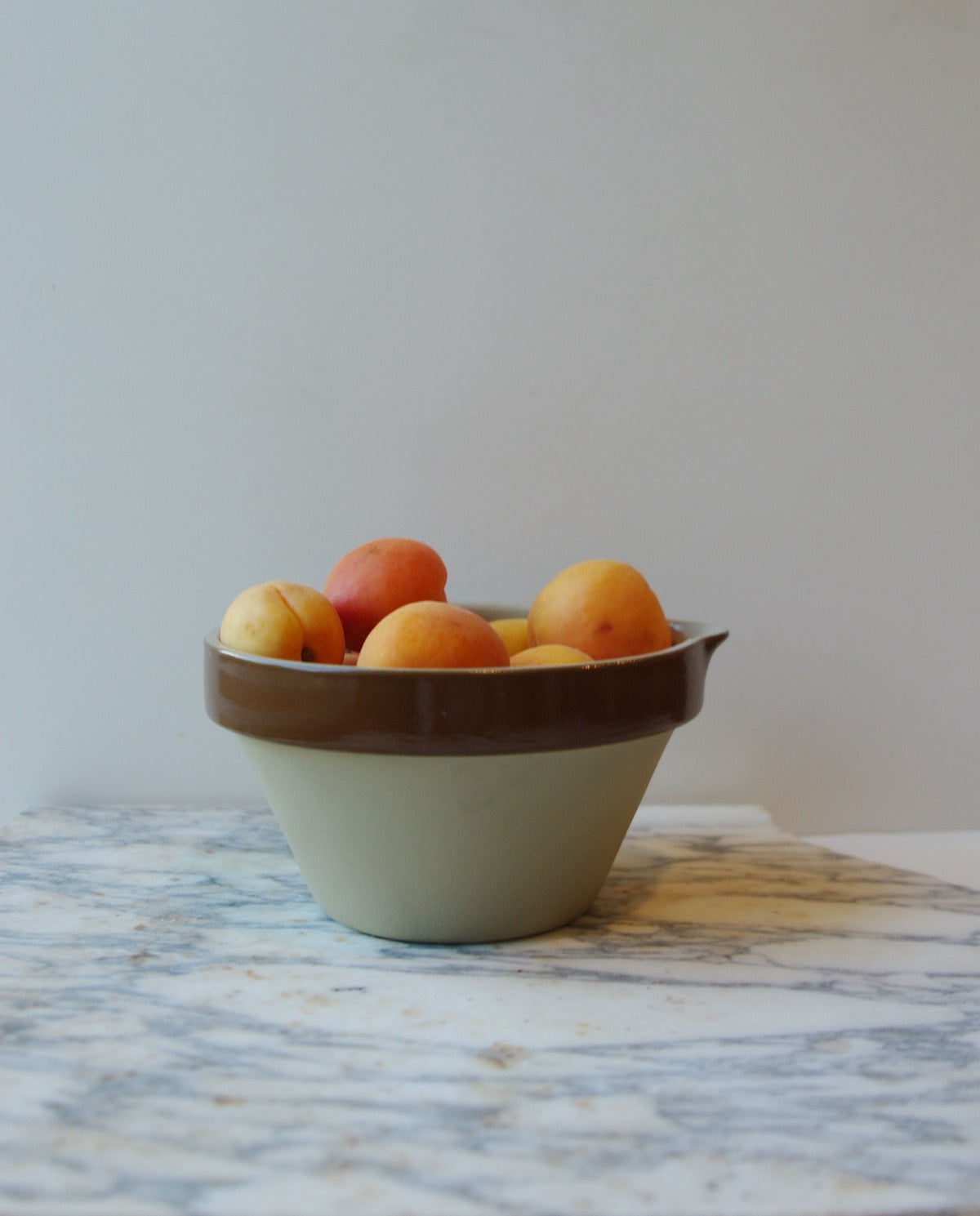 Brown and cream colored mixing bowl with spout full of orange fruit.