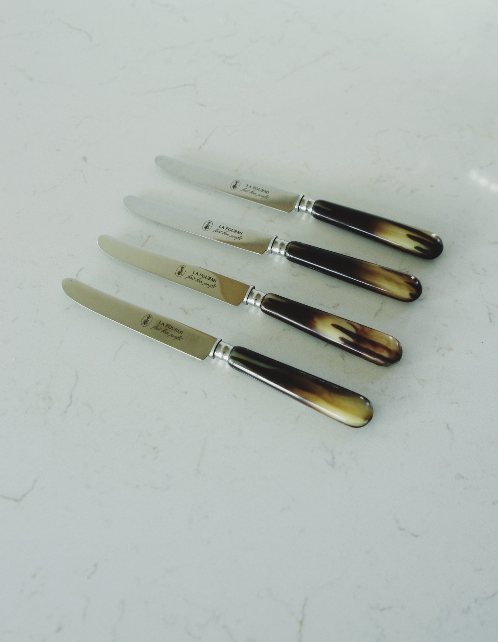 Set of vintage French dessert knives with marbled handles on a marble countertop.