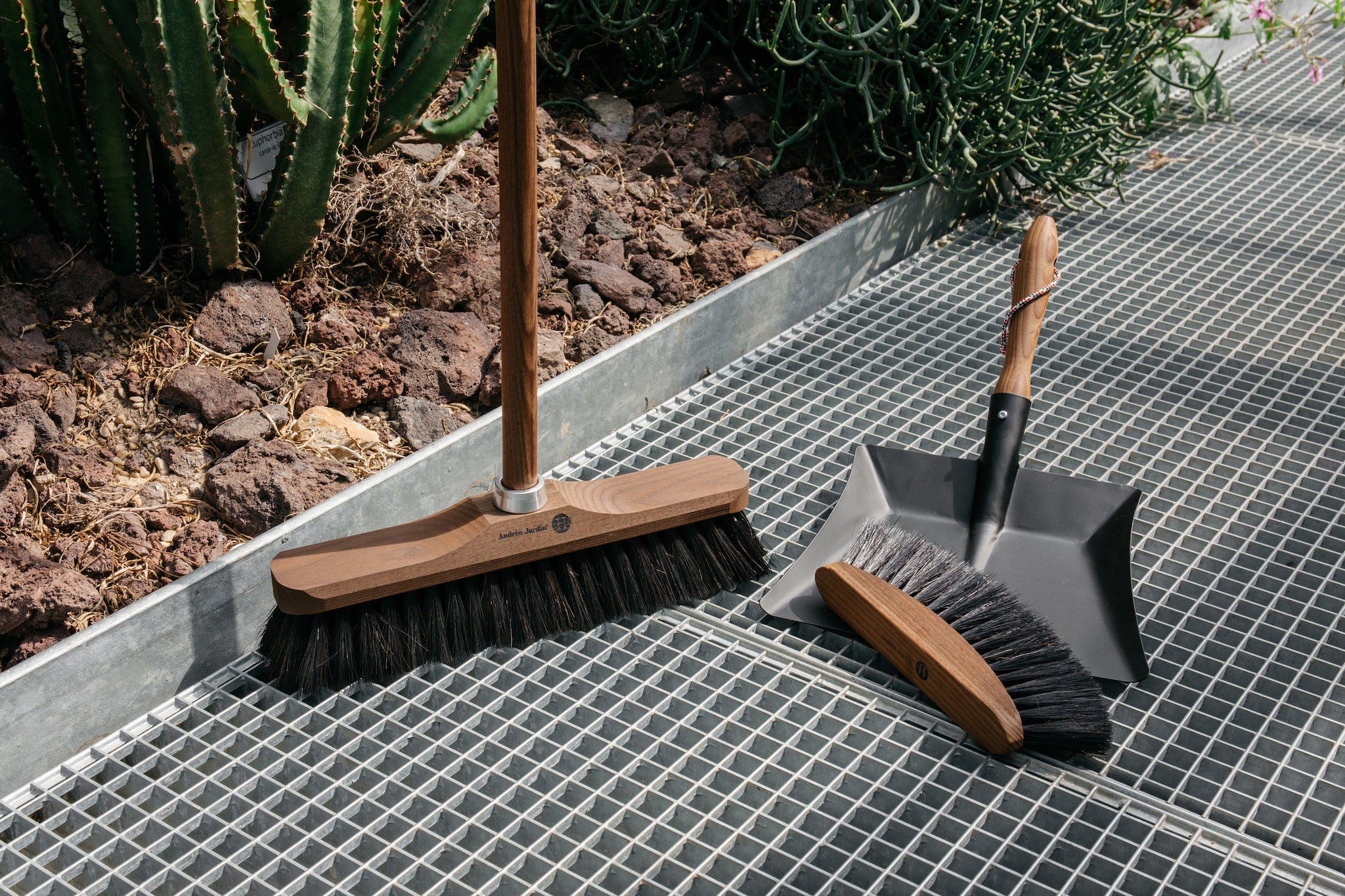 Dark wooden broom next to dark hand brush on top of black dustpan with wooden handle.