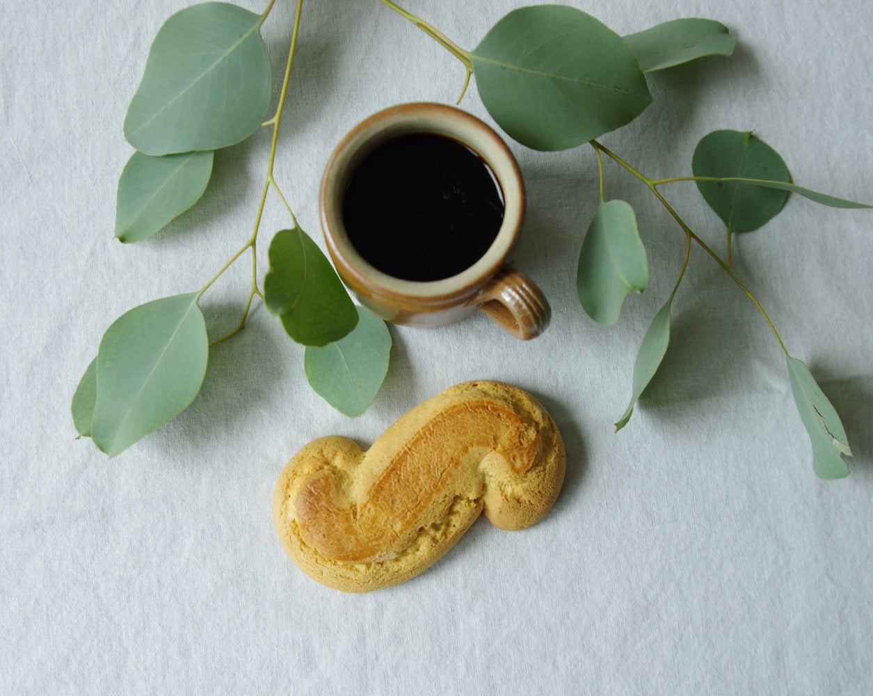 Brown mug next to pastry and eucalyptus leaves.