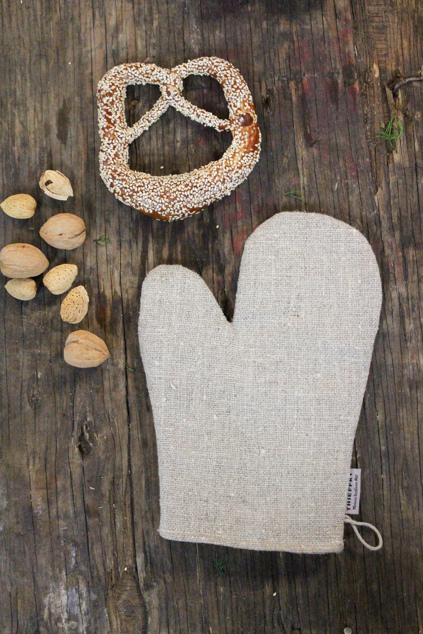 Linen oven mitt next to pretzel and walnuts on wooden table.