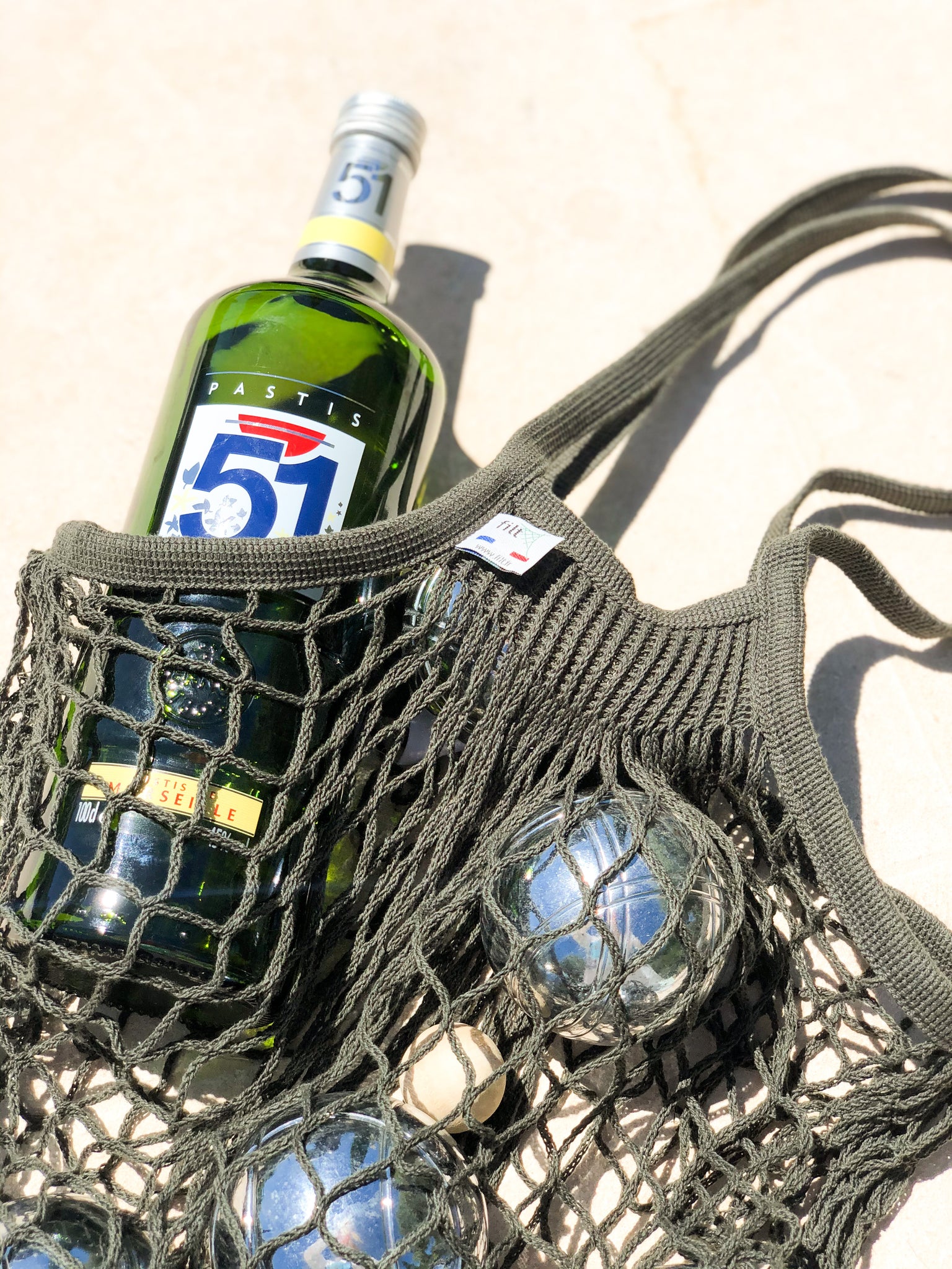 Dark olive green net bag holding petanque balls and bottle of Pastis.