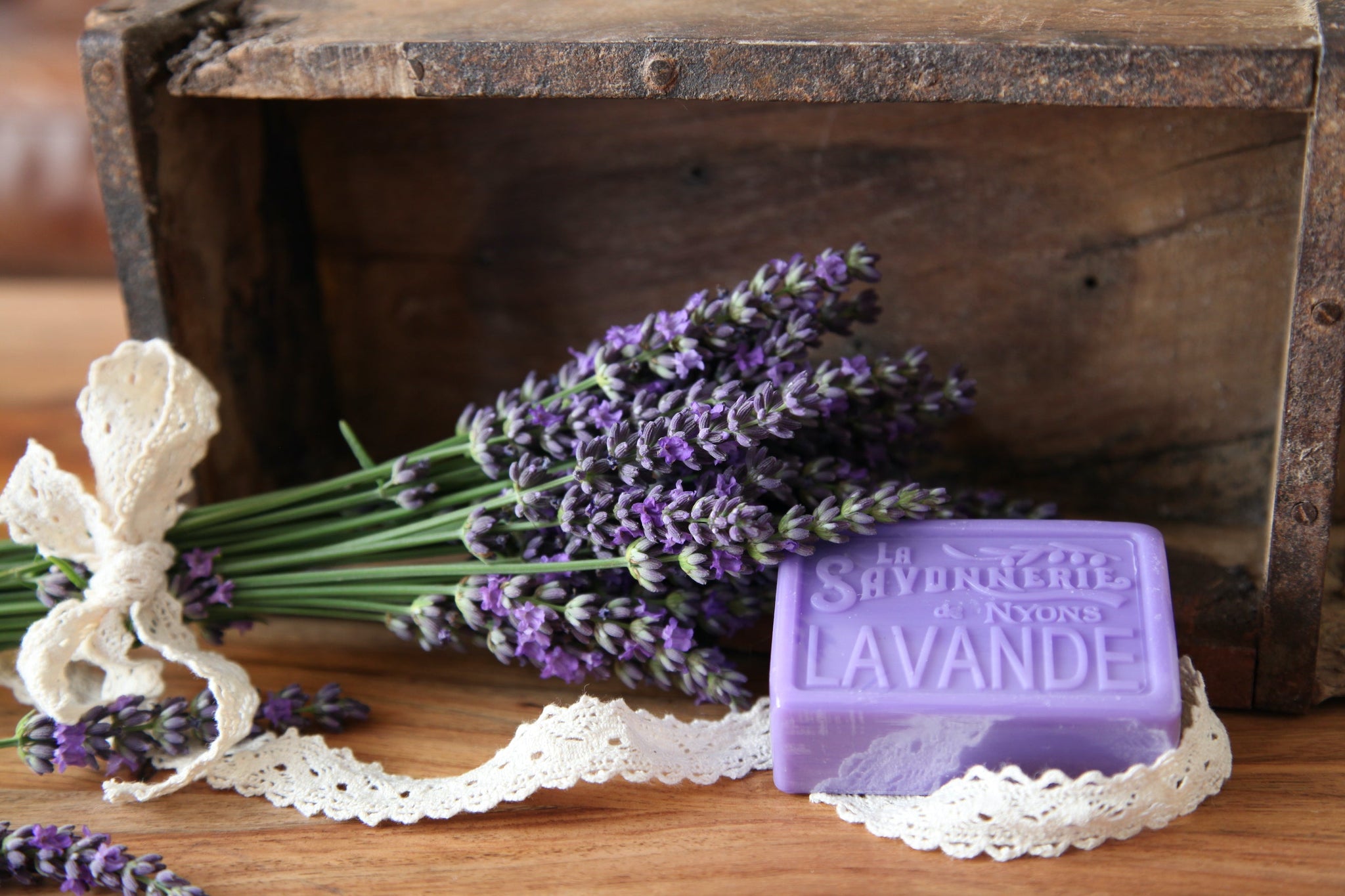 Purple bar of soap with stamp reading La Savonnerie de Nyons Lavande next to a bundle of lavender stems wrapped in lace ribbon.