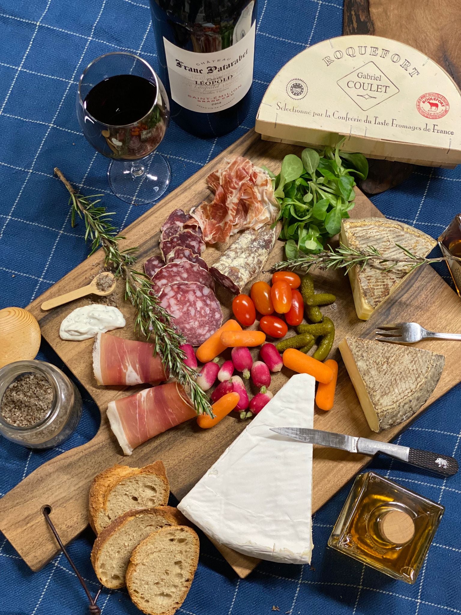 Walnut serving board with charcuterie on top next to glass of wine.
