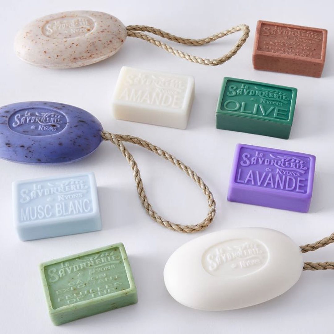 Bars of soap with stamp reading La Savonnerie de Nyons. Some of the soap bars are oval shaped and have natural rope in a loop sticking out of the soap.