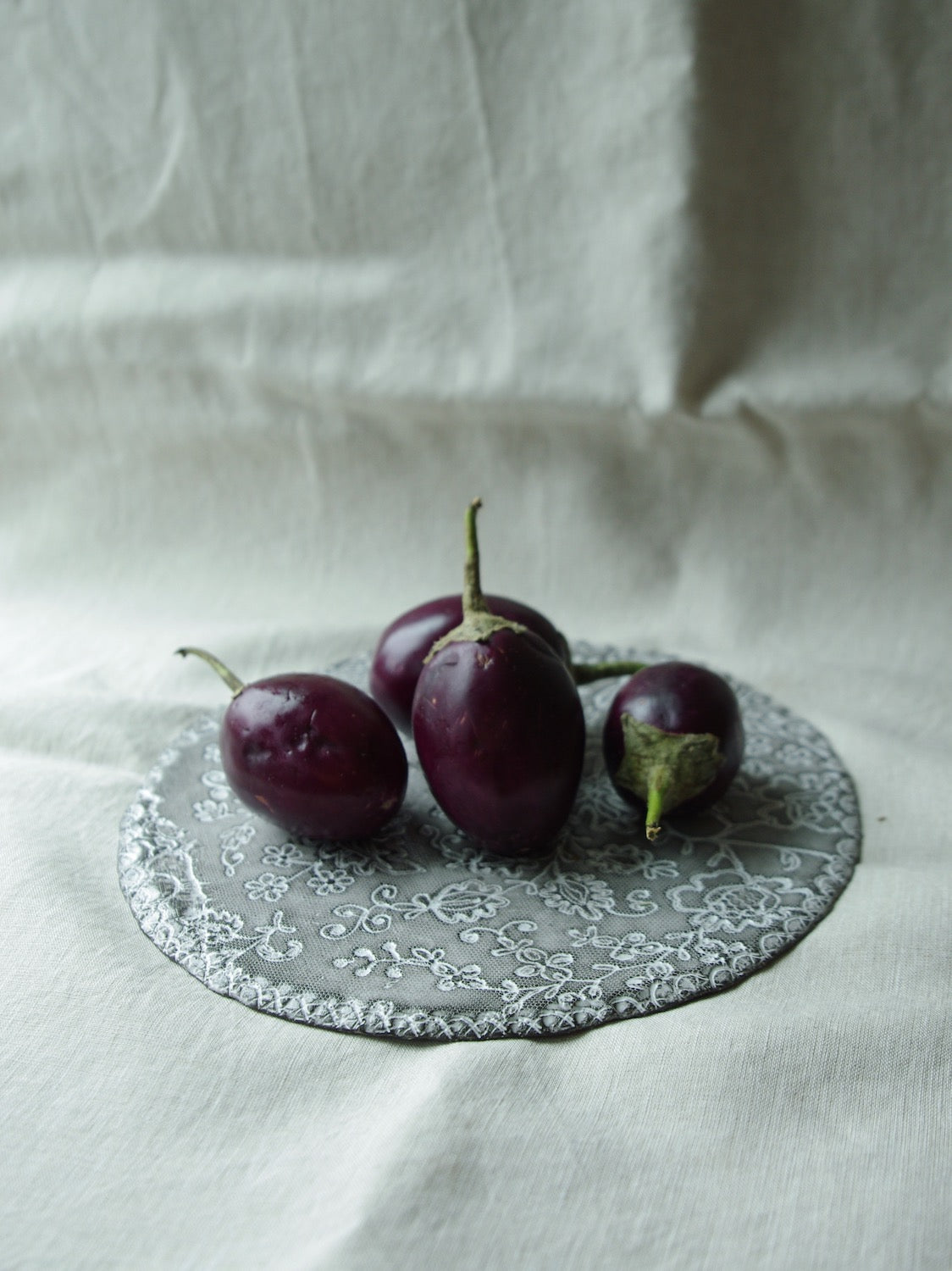Baby eggplants sitting on lace pattern ceramic plate
