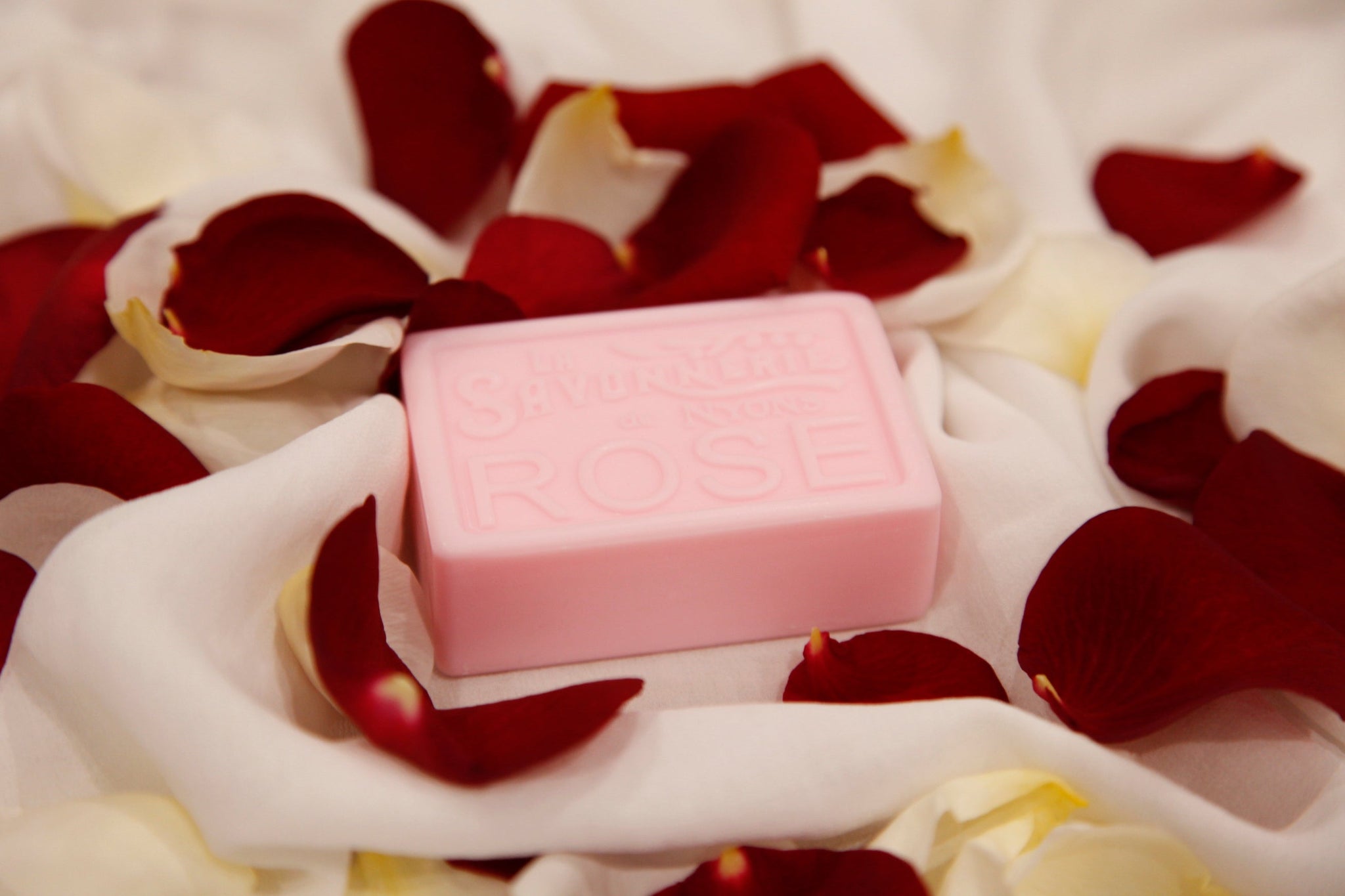 Pink bar of soap reading La Savonnerie de Nyons Rose surrounded by rose petals.